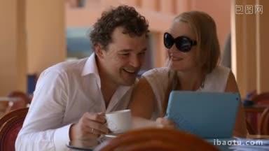 男人和女人在平板电脑上看照片，喝茶和接吻